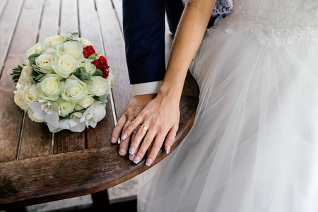 新娘和新郎的手在桌上的白色玫瑰和兰花的戒指和花束