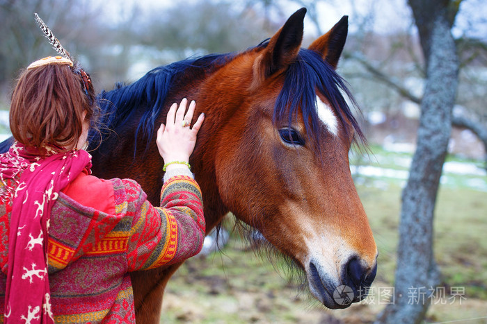 肖像女人和马在室外。抱着一匹马的女人，在她的头发有羽毛