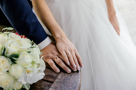 新娘和新郎的手在桌上的白色玫瑰和兰花的戒指和花束
