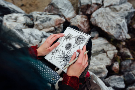 艺术家画坐在悬崖上，岩石上的女孩记事本。美好的秋天视图