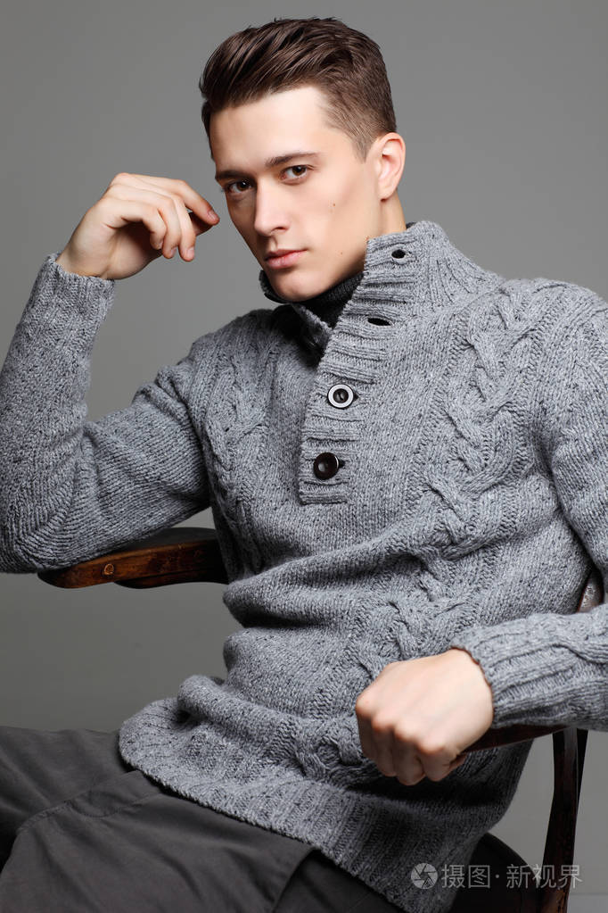 性感的年轻男子在温暖针织 sweateron 灰色的背景.男模特