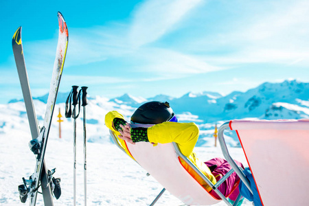 图片从妇女的后面在扶手椅, 滑雪板, 棍子在雪山度假胜地
