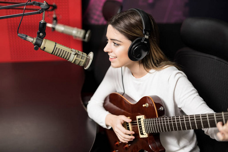 年轻女歌手在广播电台演奏吉他和唱歌在话筒