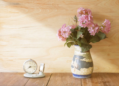 粉红色的花在花瓶和木制背景上的老式时钟