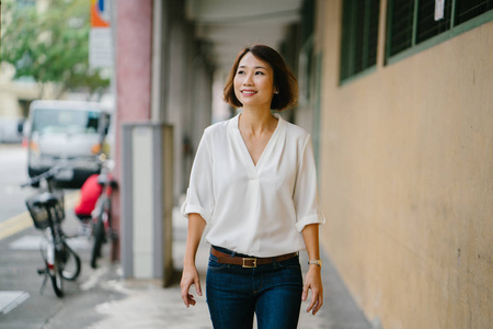 中国年轻的亚洲妇女沿着新加坡亚洲的走廊散步。她穿着巧妙的商业休闲, 短发和微笑, 她漫步在走廊上