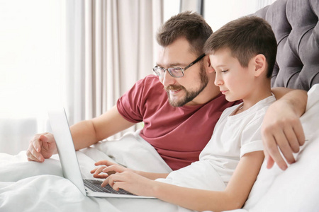 小男孩和他的爸爸在卧室里使用笔记本电脑