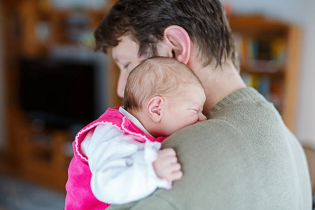 快乐骄傲的年轻父亲抱着他睡着的刚出生的婴儿女儿