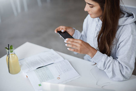 伤心的学生用手机迷人的学生的侧面看她的笔记用智能手机拍照, 坐在她