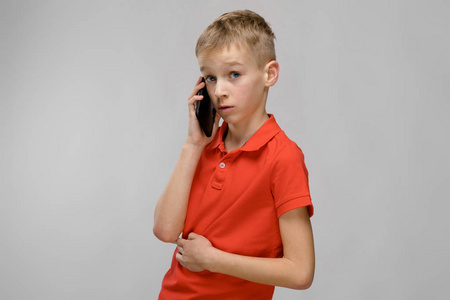 可爱的金发白种青春期男孩在明亮的 t恤显示不同的表达式, 而在工作室白墙上的电话交谈