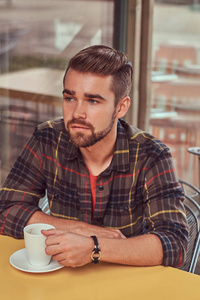 一个英俊时髦的男人, 有时髦的发型和胡须, 穿着羊毛衬衫, 在自助餐厅喝咖啡。