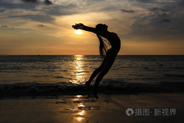 女子跳跃和在海滩上的乐趣与日落