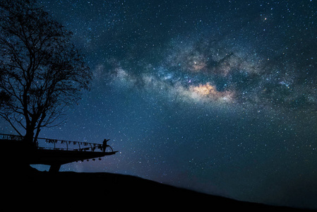 银河在夜间。五颜六色的夜空与星星和剪影的一个站在快乐的人在山上举起武器。自由旅行在长的周末假期