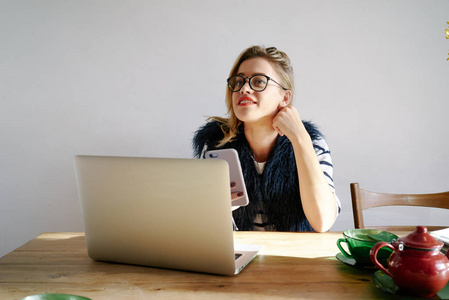 一个年轻的妇女使用智能手机的肖像坐在桌子上的笔记本电脑