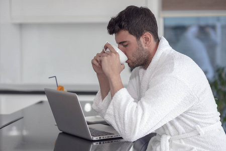 一名男子用一台笔记本电脑在家里的一件袍子