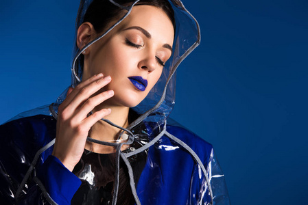 被涂污的口红蓝色口红的梦幻女郎穿着雨衣在蓝色背景下被隔离照片