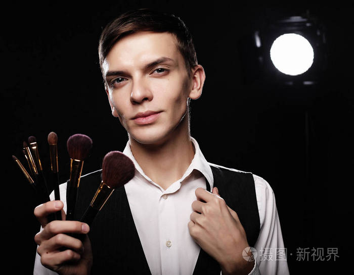 年轻的男性化妆师在黑暗中化装刷