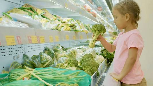 在杂货店里选择绿色蔬菜的小可爱的孩子女孩