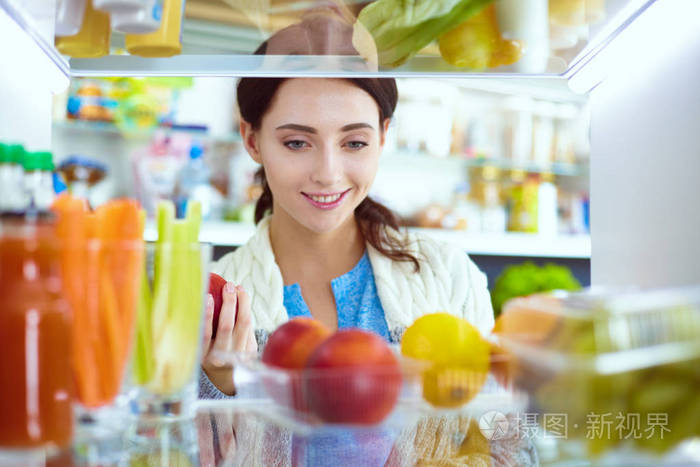 女性站附近打开冰箱充分的健康食品，蔬菜和水果的画像。女性肖像