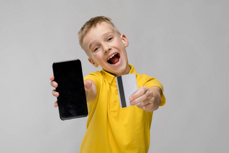 可爱的金发白种青春期男孩在明亮的 t恤显示不同的表达式和手持智能手机与信用卡在演播室白墙