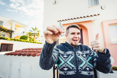 一个快乐的年轻人伸出新房子的钥匙和打手势拇指向上的肖像