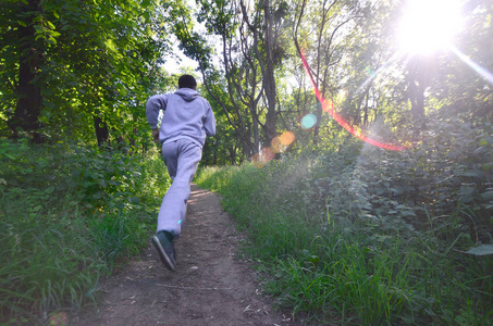 一个穿着灰色运动服的年轻人沿着树林里的树林走来走去。户外运动慢跑