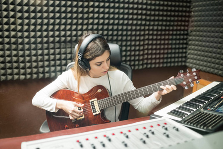 戴着耳机弹吉他的女人在隔音录音室准备新的音轨