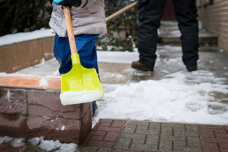 孩子帮助父亲清除人行道上的积雪。坦率正宗的家庭冬季活动。铲雪概念