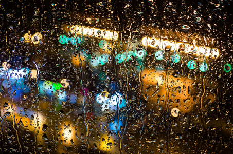 雨滴在玻璃和夜间城市的灯光