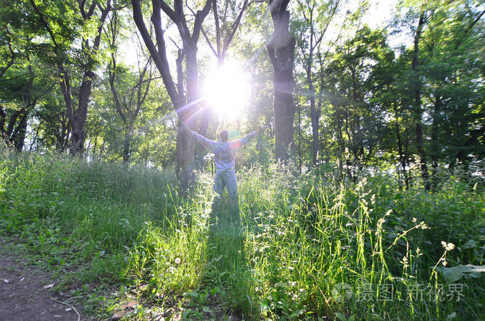 一个穿着灰色运动服的年轻人在森林里的树上晒太阳.