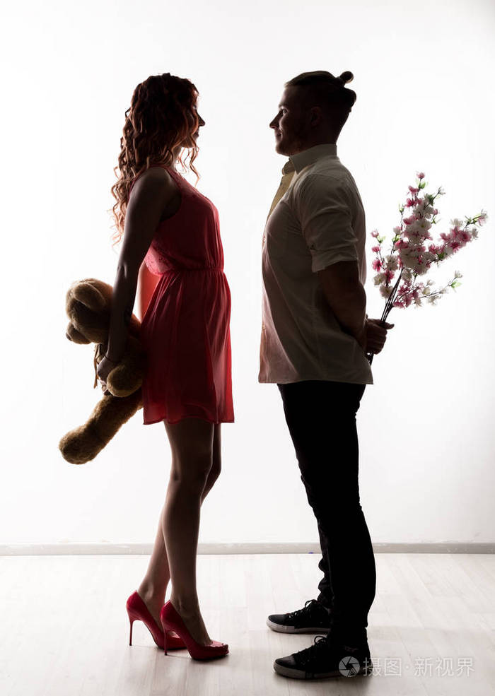 和男人约会的女孩男人捧着花和女人抱着泰迪熊.光线背景下的剪影
