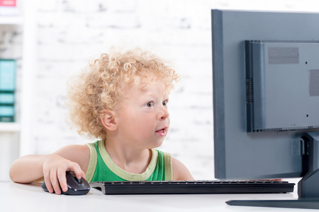 一个小小的卷曲金发男孩，玩电脑
