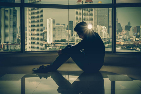 摩天大楼窗户沮丧的人坐在手在室内摩天大楼与低光环境旁边的窗户上空