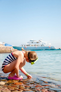 条纹的泳衣和掩码在海岸上的小船的背景上玩浮潜的女孩