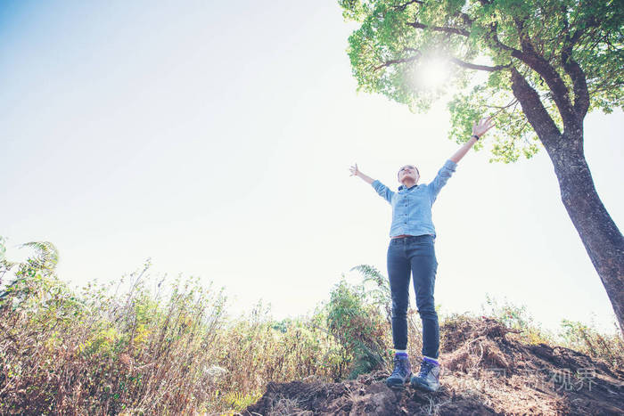 年轻女子站在仰望天空, 举起手, 而在山上远足