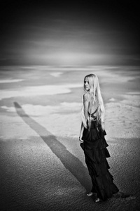 一个年轻的金发女郎穿着黑色的长裙走在沙漠里