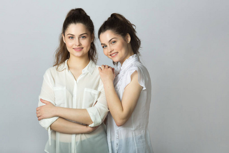 两个美丽的微笑的女孩姐妹双胞胎在白色上衣在轻的背景下