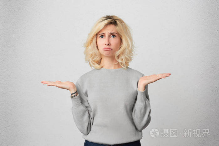 室内的镜头中, 疑惑的金发女郎, 耸耸肩, 有犹豫的表情, 穿着灰色的
