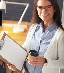 年轻女人站在桌子旁边与笔记本电脑拿着文件夹和杯咖啡