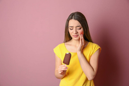 有敏感牙齿的妇女在彩色背景下持有冰淇淋