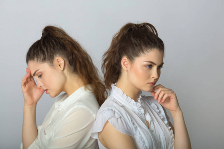 两个美丽的姐妹双胞胎女孩与严重的面部表情在白色上衣的光背景