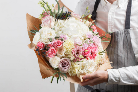 美丽的花束不同用花卉做成的年轻人手中。缤纷的色彩组合花。工作服装穿着白衬衣，灰色的围裙