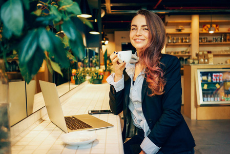 一个可爱的女人的肖像工作与笔记本电脑和咖啡店喝咖啡