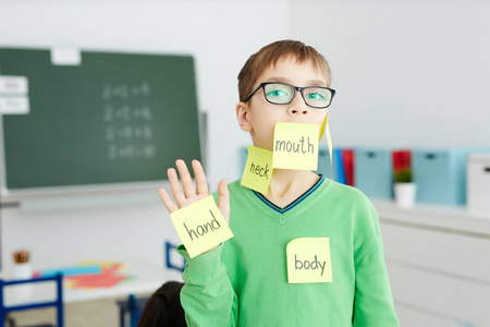 学生在眼镜与身体部分名称写在 notepapers 卡住在他的手和脸上