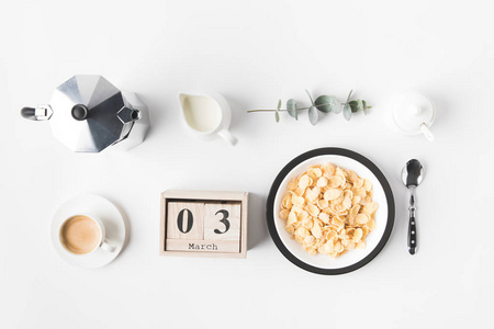 平躺在碗里的玉米片在早餐, 咖啡壶和日历白色表面