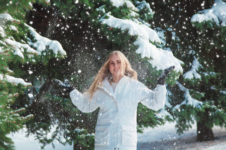 年轻开朗的女人在户外玩得开心。在最冷的冬天背景下的树和雪。女孩穿着一件白色外套和黑色手套