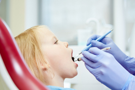 儿科牙医检查在牙医的椅子上的小女孩牙齿。