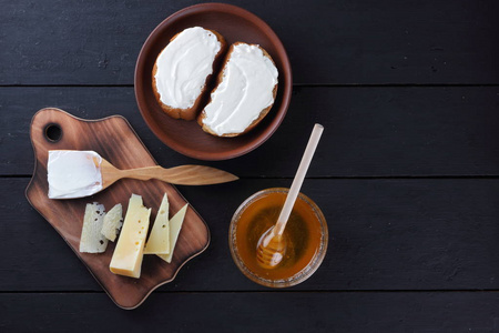 硬奶酪的木板, 三明治与软奶酪, 蜂蜜在玻璃菜, 复制空间, 简约主义, 奶酪图案, 木质深色背景, 健康食品, 木制餐具