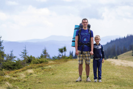 父亲和儿子带着背包徒步漫步在风景秀丽的夏绿山上。爸爸和孩子站在欣赏山水山景。积极的生活方式, 家庭关系, 周末活动的概念