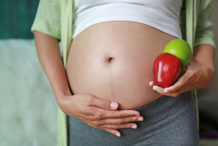 怀孕妇女在她的腹部拿着绿红苹果果。健康的生活方式