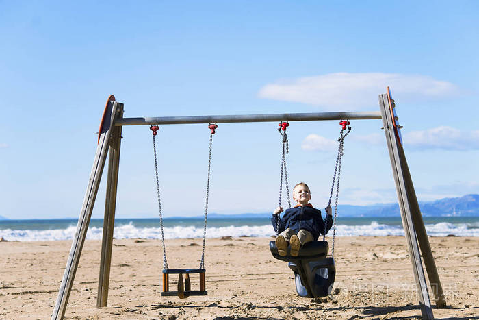男孩在春天在海滩上骑木秋千